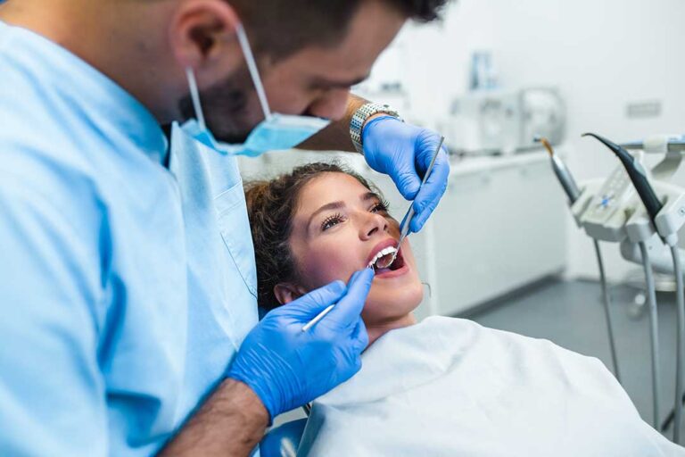 A person checking their teeth and gums in a bathroom mirror under bright lighting.